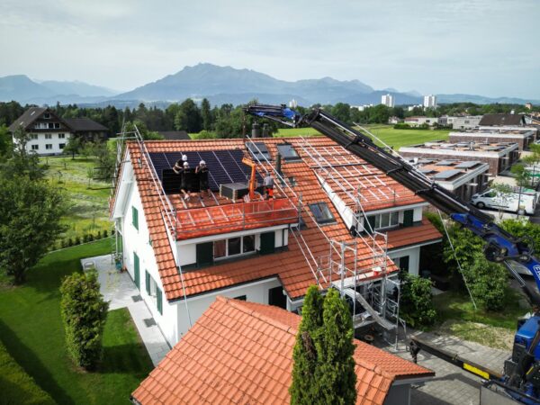Blick über ein Einfamilienhaus mit halb montierter Photovoltaik-Anlage und dem Kranwagen auf der Strasse.