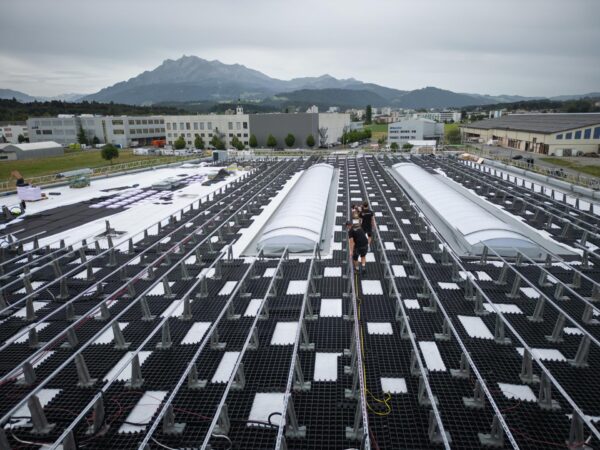 Grosse Photovoltaik-Anlage auf einem Industrie-Flachdach, im Hintergrund die Berge.