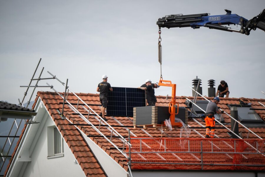 Zwei Monteure nehmen ein Modul vom Kranhaken, im Hintergrund die Berge der Zentralschweiz.