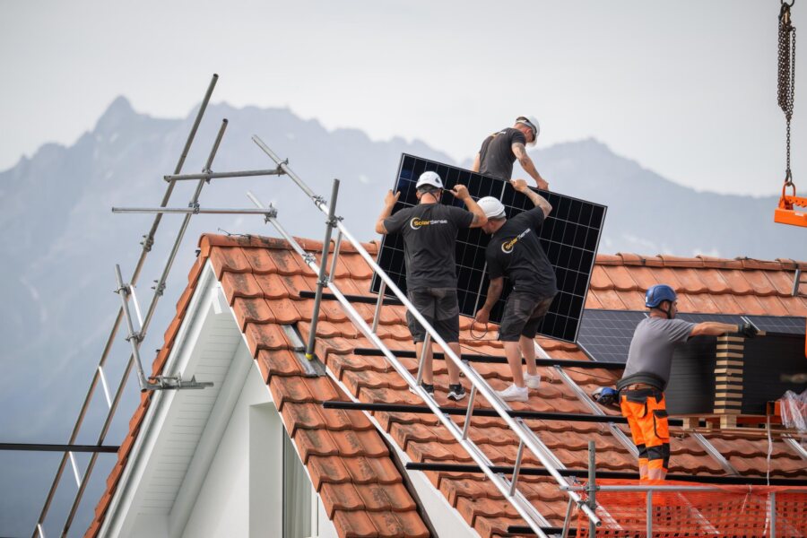 Das Montageteam richtet ein Photovoltaik-Modul auf dem Dach aus, im Hintergrund die Berge.