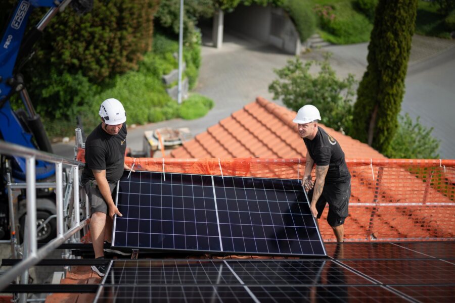 Zwei Monteure setzen ein Photovoltaik-Modul auf die Dachschienen.