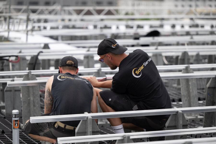 Zwei Monteure verschrauben auf dem Flachdach eine Aluminium-Schiene.
