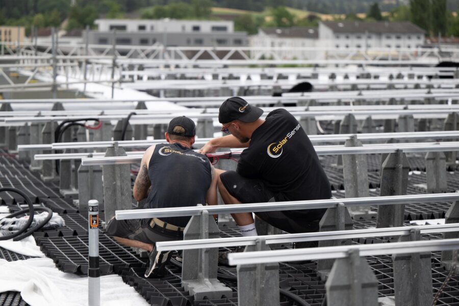 Zwei Monteure montieren auf dem Flachdach die Aluminium-Schienen der Unterkonstruktion.
